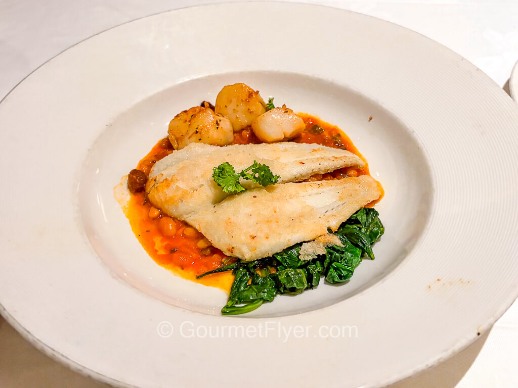A piece of grilled white fish is served with a red sauce and vegetables.