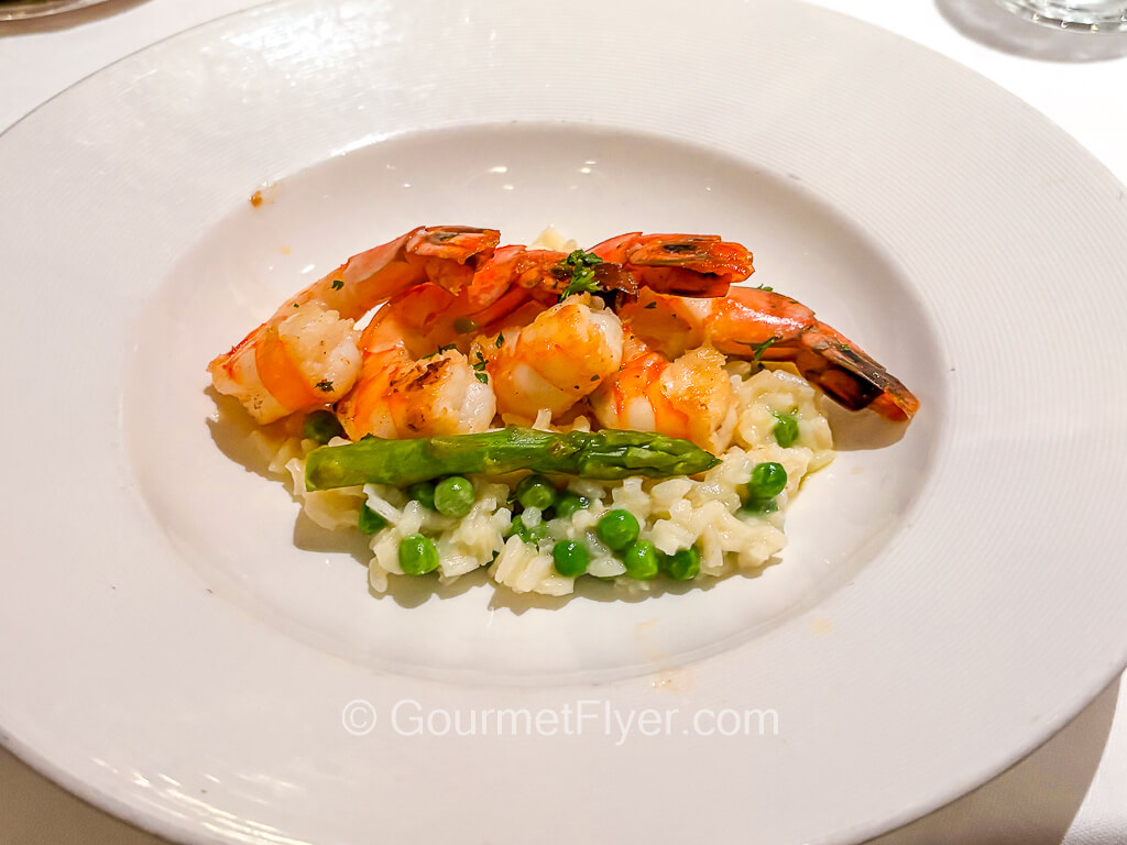 Large, cooked shrimps are served atop a bed of rice with green peas.