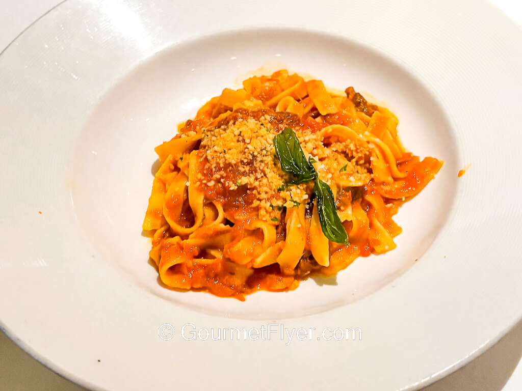 Wide fettuccini pasta is tossed in a tomato sauce and topped ith grated cheese.